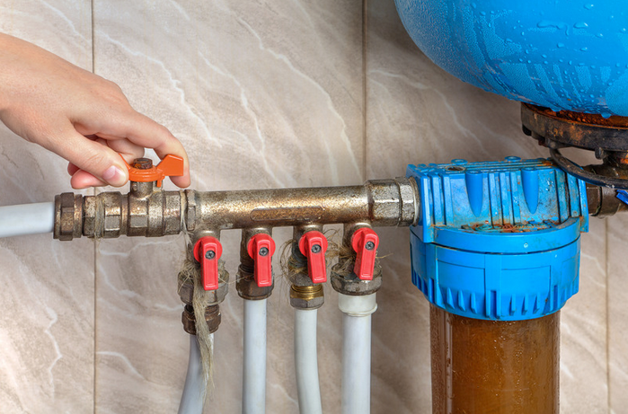 A man turning off the water supply to a kitchen sink.