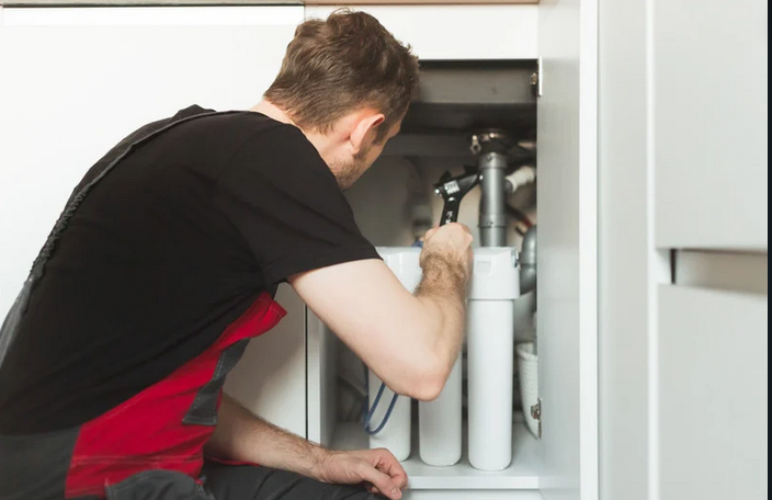 A man installing a water filtration system beneath a kitchen sink.