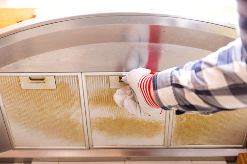 Repairman taking filthy aluminum mesh filter out of the cooker hood