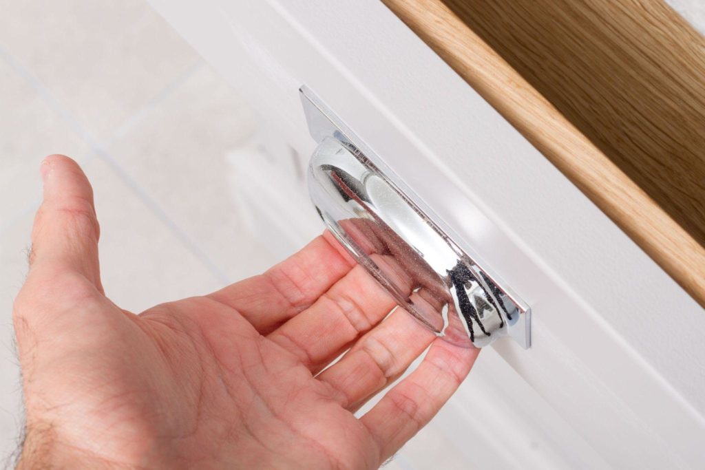 A man holding a transparent plastic pull trying to open a white kitchen cabinet drawer.